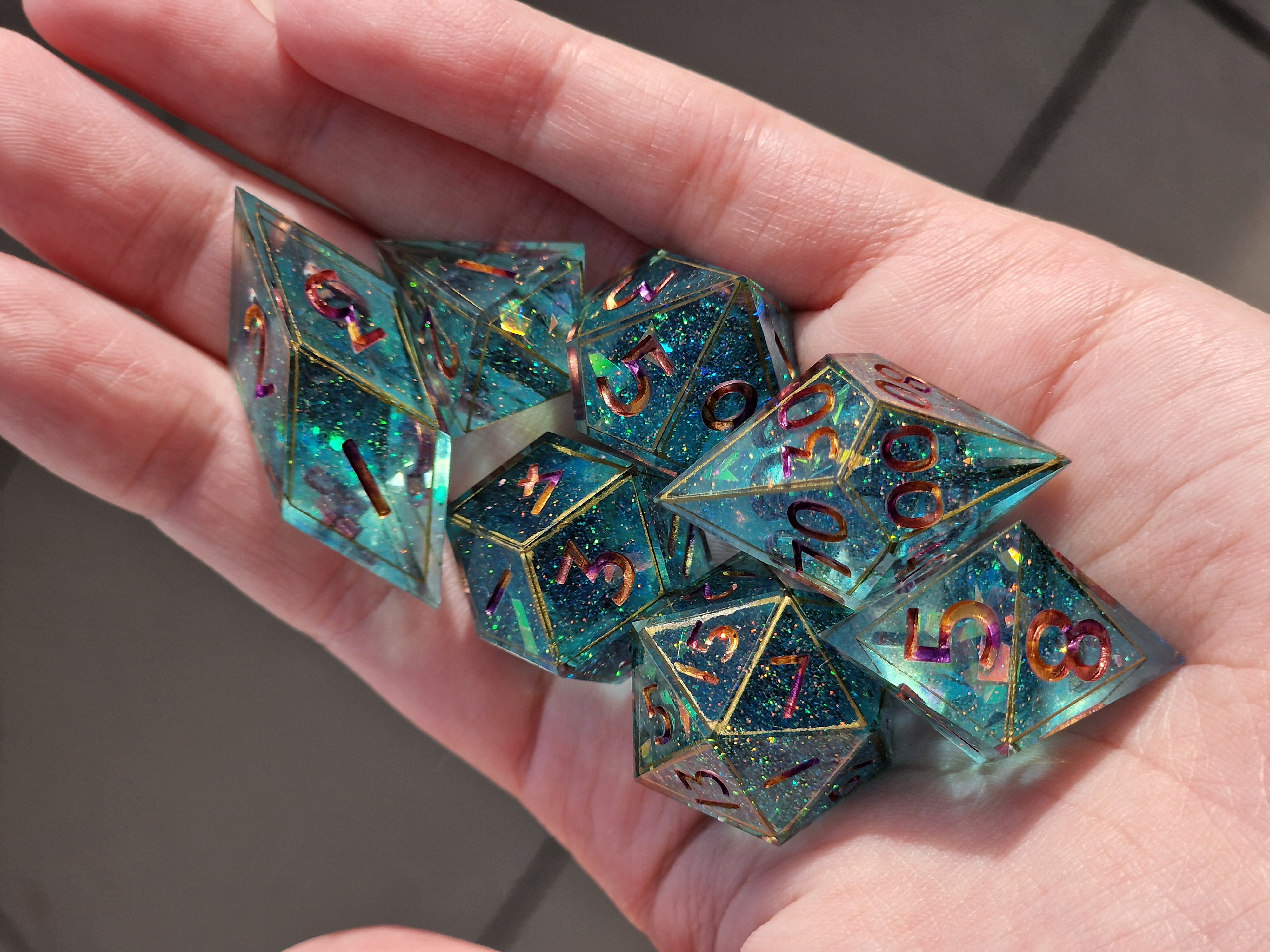 Teal crystal-clear dice shimmer with rainbow fragments, gold edges, and jewel-toned numbers.
