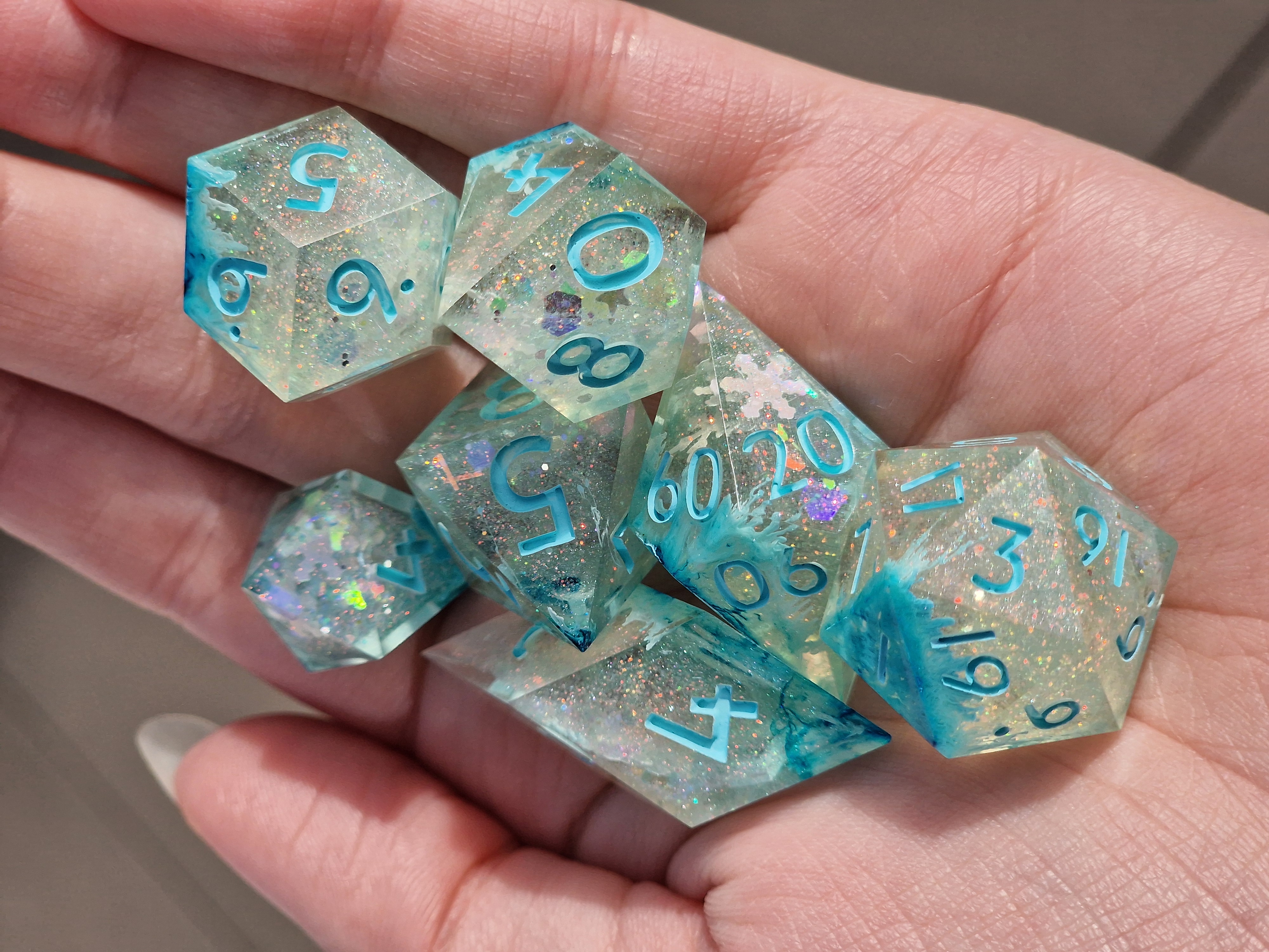 Icy blue swirls and snowflakes drift through sparkling clear dice, with bright turquoise numbers.