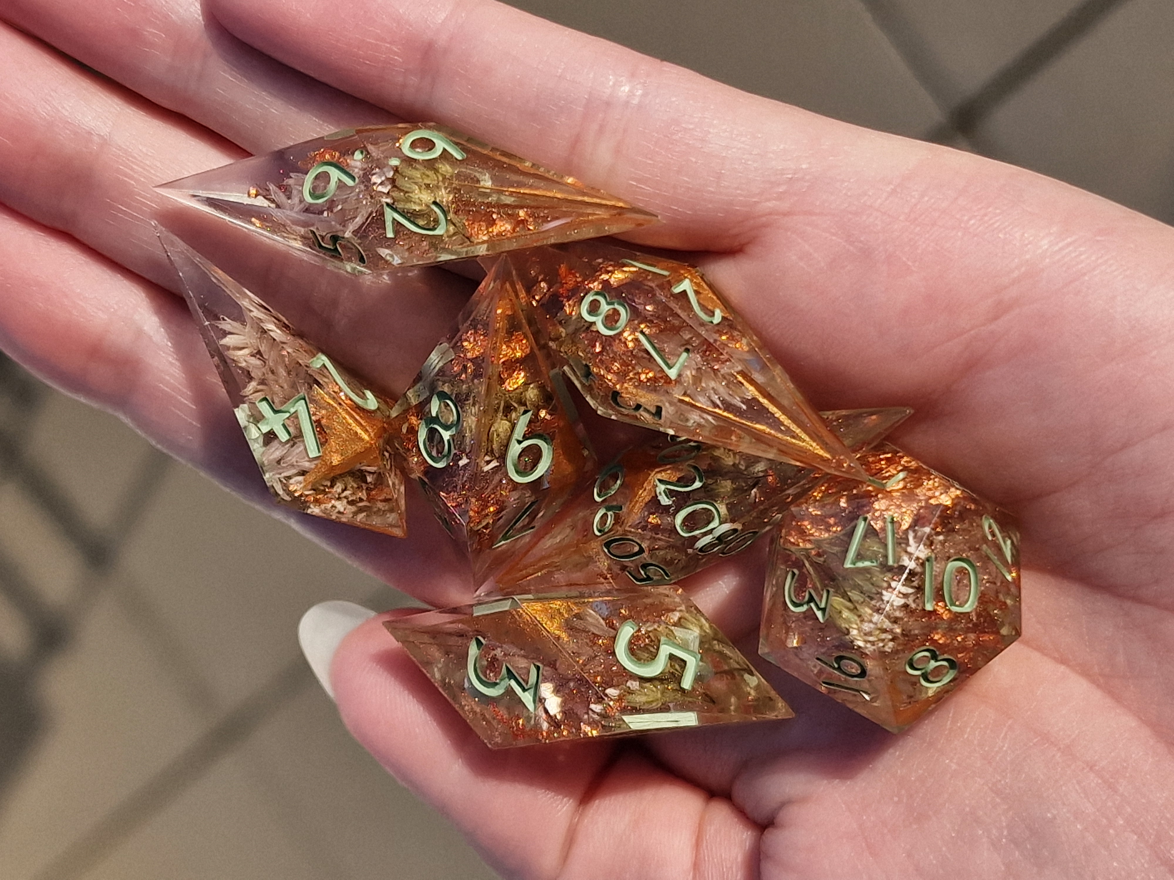 Delicate botanicals and coppery shimmer rest in amber-toned resin, finished with soft green numbers.
